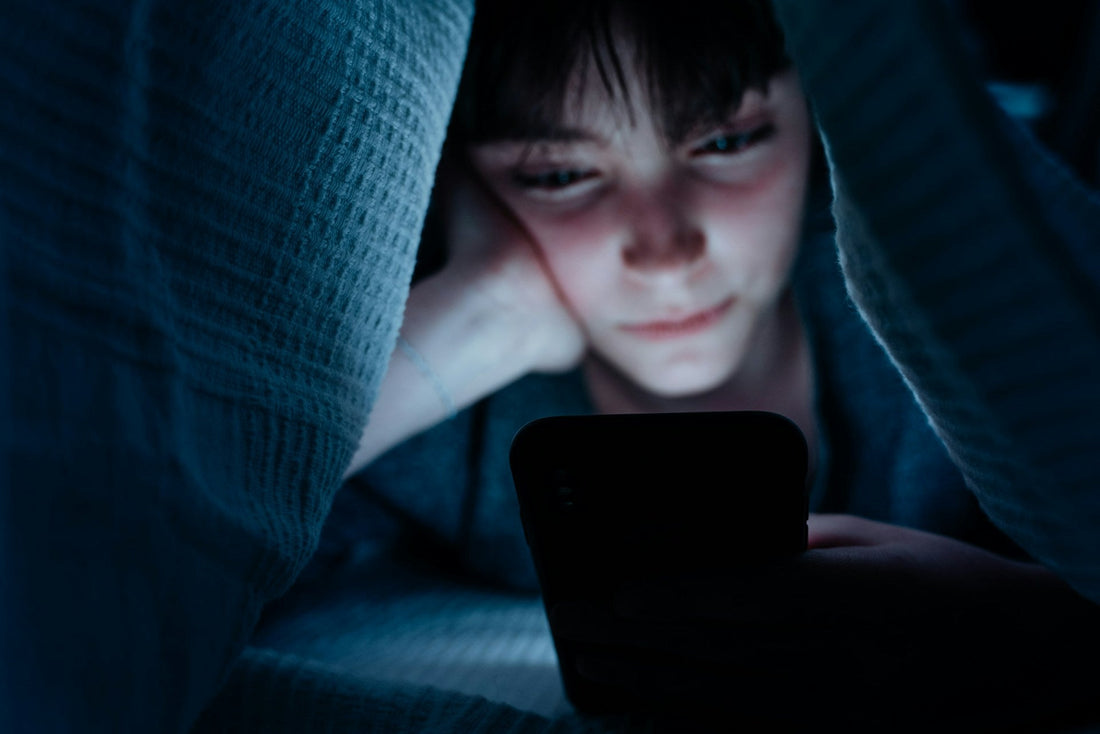 Woman lying in bed at night absorbed in her phone, representing emotional attachment and false intimacy created through texting before meeting in person.