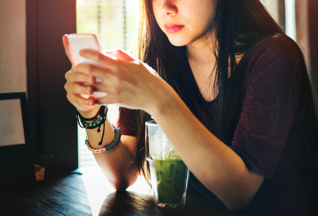 Woman looking at her phone in a café while receiving frequent messages, representing daily texting that never turns into real dating plans.