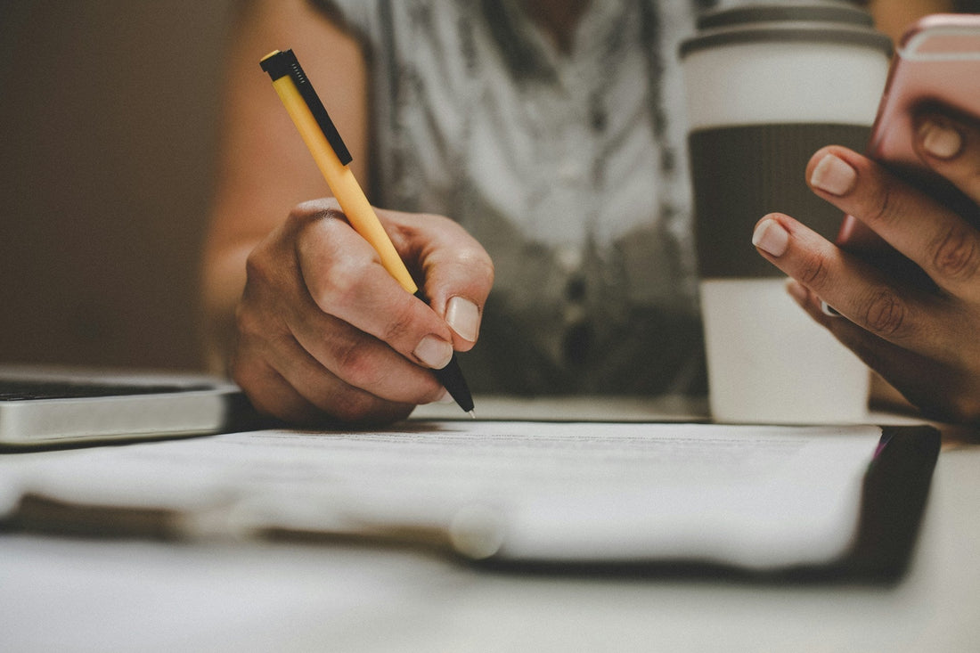Person writing in a notebook while holding a phone, reflecting on an unsent breakup letter and words they chose not to send.