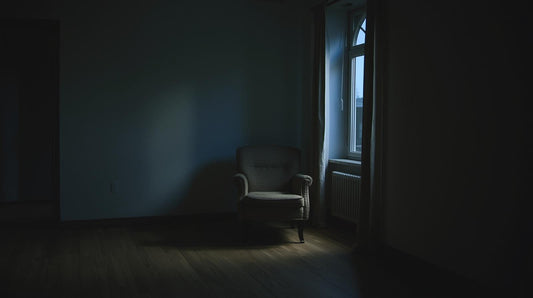 Single armchair slightly out of place in a dim apartment at dusk, symbolizing feeling unsettled when alone