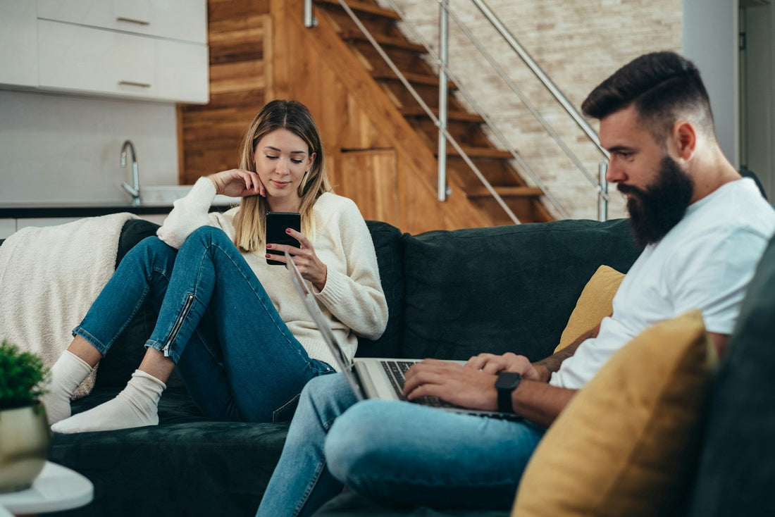 Couple sitting on a sofa distracted by their phones, representing a lack of attention, reduced quality time and emotional disconnection in a relationship.