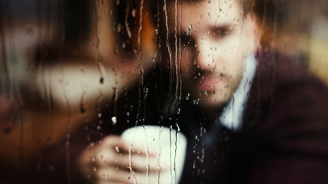 Person seen through a rain-covered window, symbolising old breakup feelings returning after they seemed to have faded.