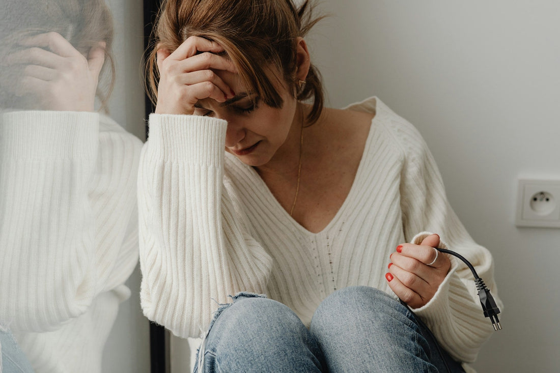 Sad Person in a white sweater holding a black cord, sitting against a neutral wall symbolizing low self esteem and feeling responsible for everyone else.