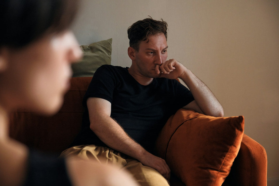 Man sitting silently across from his partner while questioning troubling behaviour and relationship red flags.