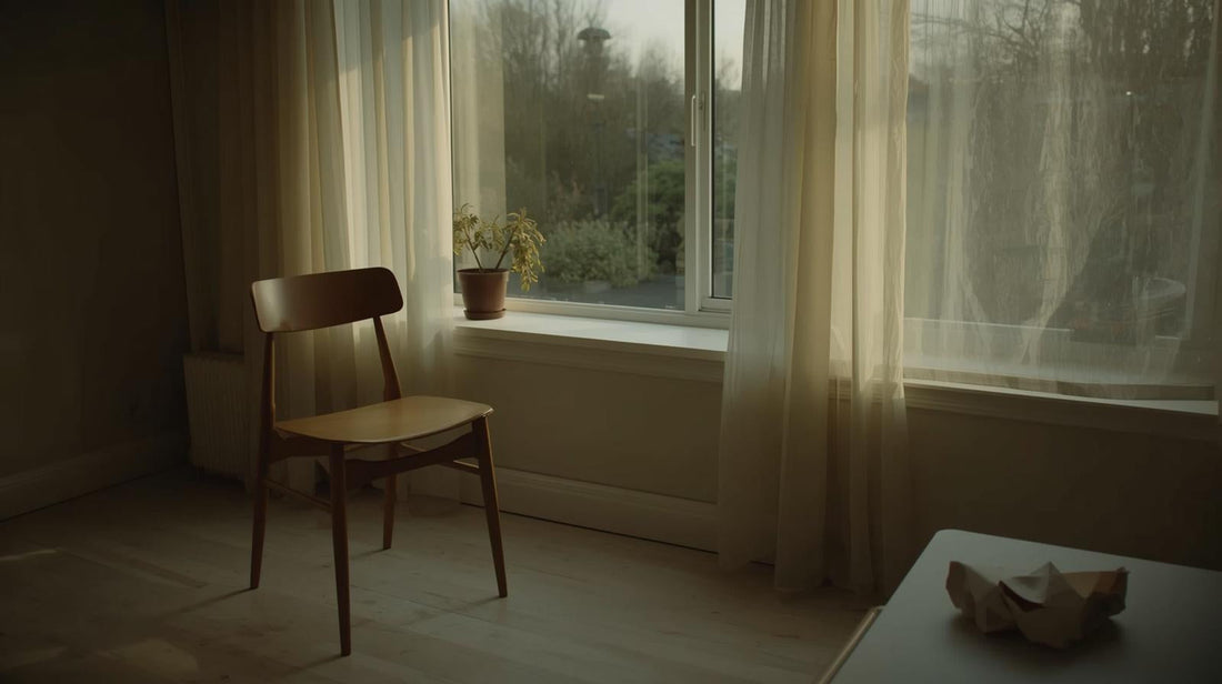 Quiet minimalist room at dusk with a chair by a window and a plant showing both green and wilted leaves, symbolizing lingering hope and emotional uncertainty
