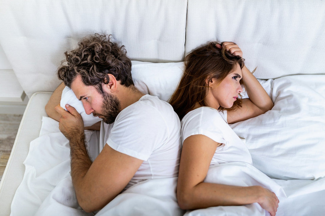 Couple lying back-to-back in bed while struggling with emotional distance and loss of sexual desire in their relationship