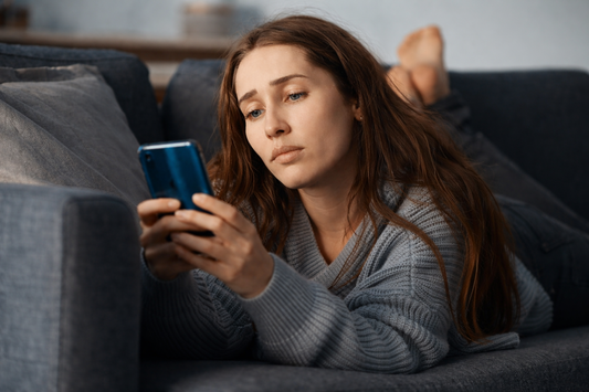 Woman lying on a sofa looking at her phone with a distant, reflective expression after a breakup