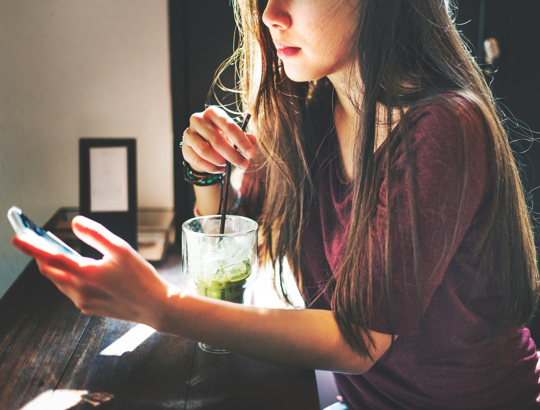 Woman looking thoughtfully at her phone in a café, representing confusion over a dry text or short reply while dating.
