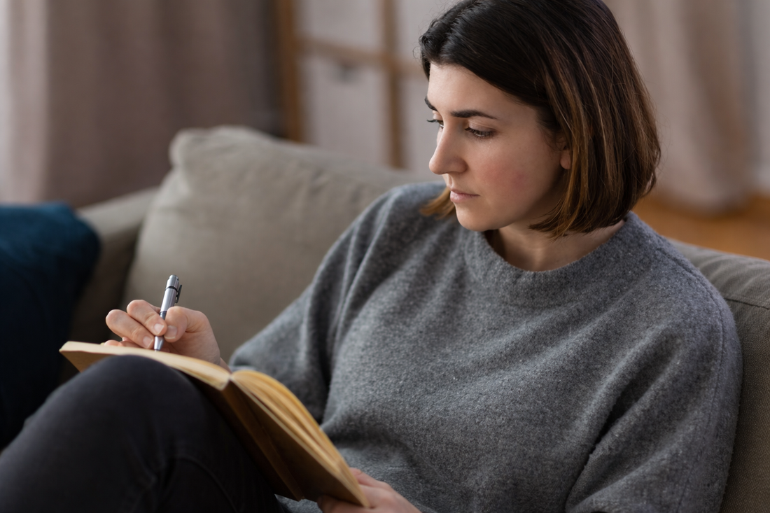 Woman sitting on a couch writing in a notebook, reflecting quietly during emotional healing after a breakup