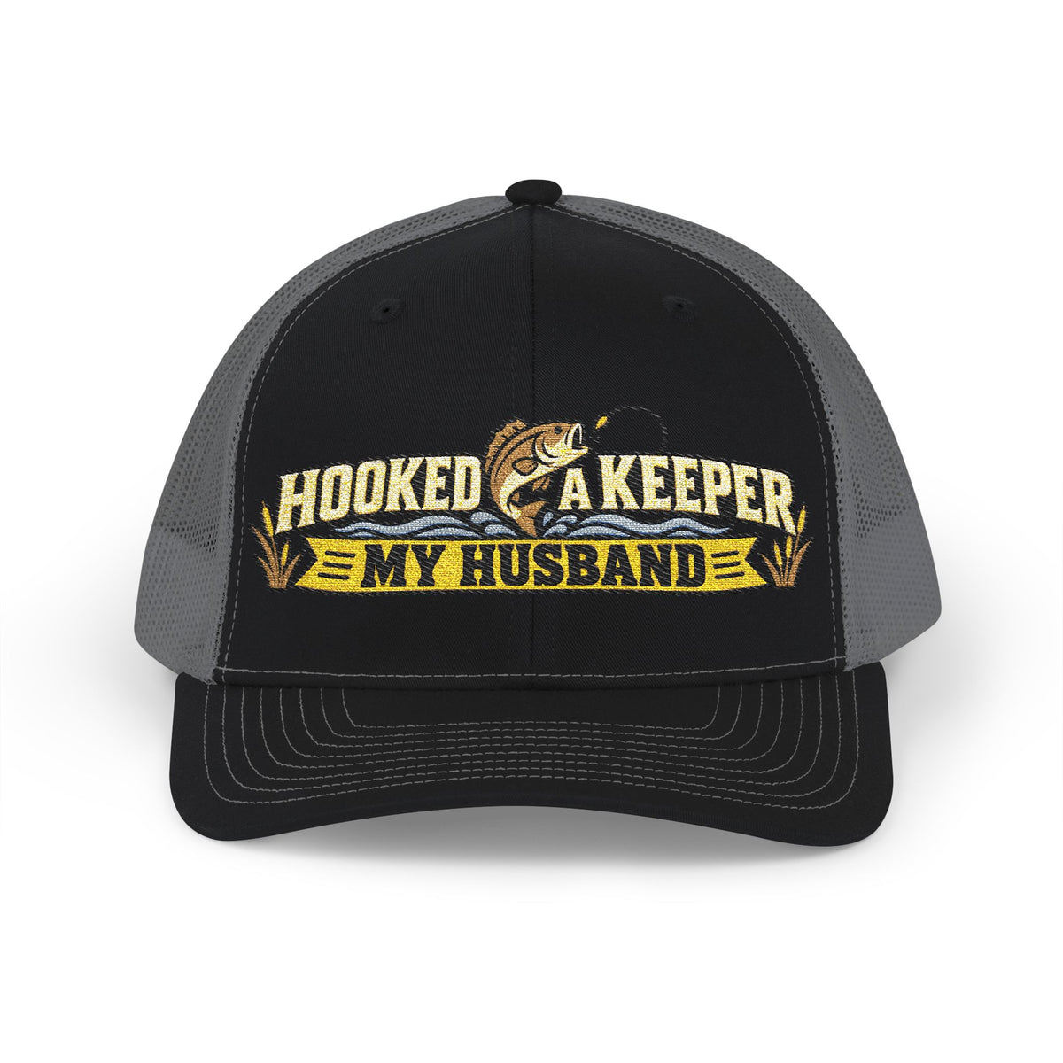 A black and gray trucker hat with a front graphic that reads 'HOOKED A KEEPER MY HUSBAND' in yellow and white, featuring a fishing rod and fish illustration.
