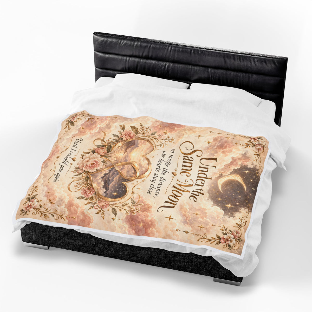 A bed dressed with a decorative throw blanket featuring a vintage-style celestial print with hearts, flowers, script text, and a crescent moon, shown on a black bed frame against a white studio background.