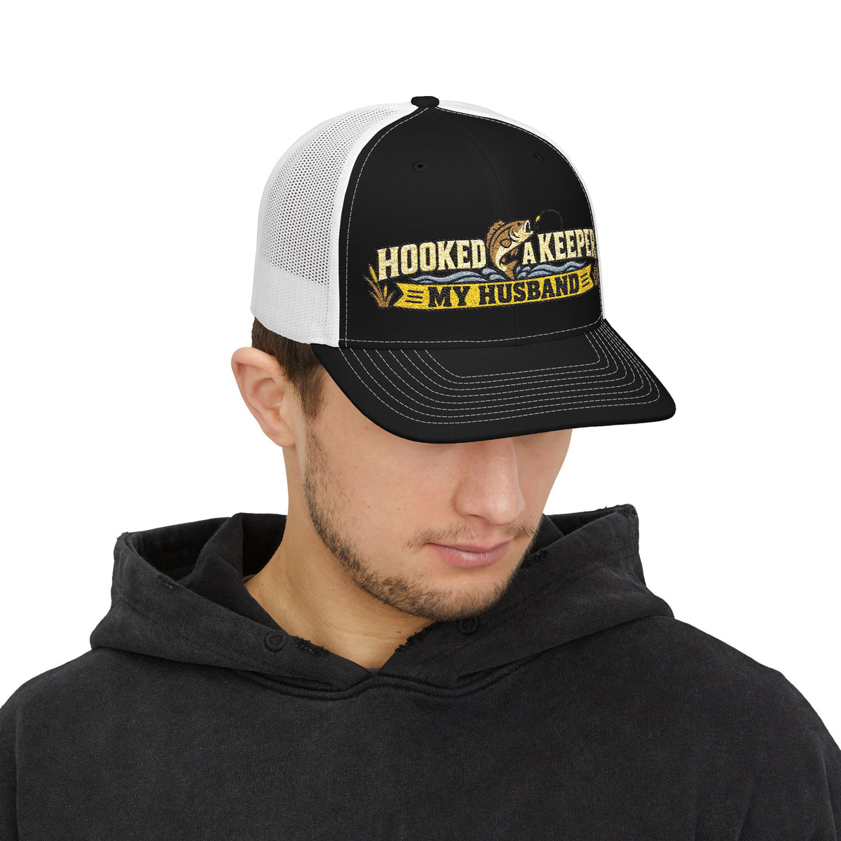 Man wearing a black and white cap with 'hooked a keeper fisherman gift logo on a white background