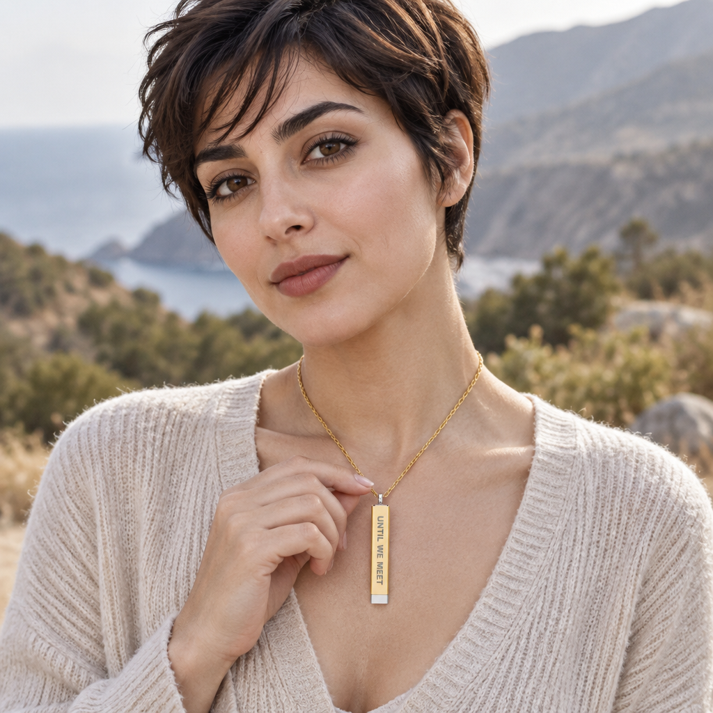 A woman wearing a gold bar pendant necklace with the words 'your text here' engraved on it, set against a scenic outdoor background of hills and water.