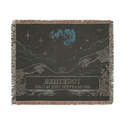 A square woven throw blanket with fringe edges, featuring a dark night-sky design with stars, a blue moon, two reaching hands, and the text 'TOGETHER NO MATTER THE MILES' on a white background.