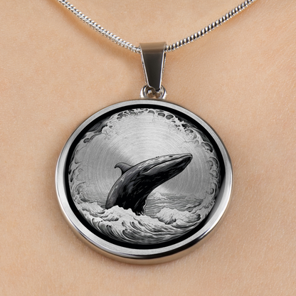 A silver round pendant necklace featuring a detailed black and white illustration of a whale jumping from the ocean, shown worn on a person's skin.