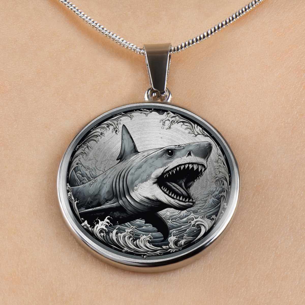 A silver round pendant necklace featuring a highly detailed engraving of a shark swimming through ocean waves, shown worn on a person's neck against a light skin tone background.
