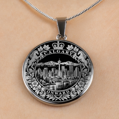 A round silver pendant necklace featuring an engraved Calgary cityscape with mountains, skyline, water, and decorative floral borders, shown worn on a person's neck against a light skin tone background.