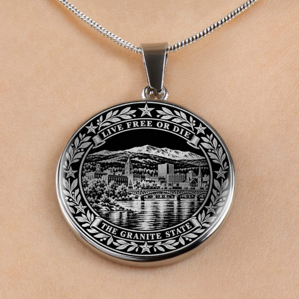 A silver round New Hampshire pendant necklace featuring an engraved black-and-white scenic design with the text 'LIVE FREE OR DIE' and 'THE GRANITE STATE,' shown worn against a light skin tone background.