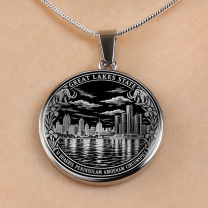 A silver oval pendant necklace featuring an engraved Great Lakes State Detroit cityscape and skyline, shown worn on a person's neck against a light skin tone background.