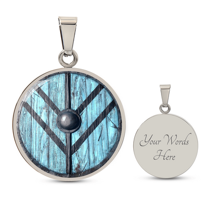 Viking shield necklace featuring a weathered turquoise-blue round shield with dark reinforcing bands and central metal boss on a circular pendant with engraving option.