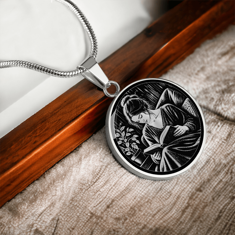 Silver-colored round book lover necklace with black-and-white linocut-inspired illustration of a woman reading indoors.
