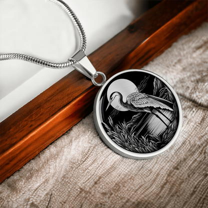 Heron necklace featuring a long-legged wading bird beside a marsh with reeds and trees in detailed black-and-white artwork on a round pendant.