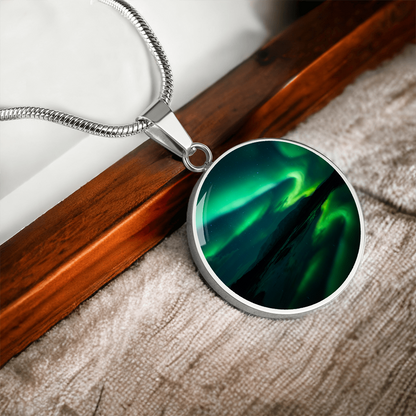 Green Aurora Northern Lights necklace featuring vivid emerald aurora ribbons above dark mountains on a round silver-colored pendant with wood background