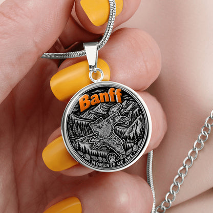 Silver Banff mountain necklace featuring orange Banff lettering, black-and-white Rocky Mountain forest artwork, paw-print symbol and Moments of Awe inscription