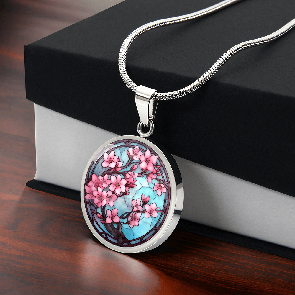 Cherry blossom necklace featuring pink sakura flowers on dark branches against a turquoise-blue stained-glass-style circular pendant. Silver with gift box