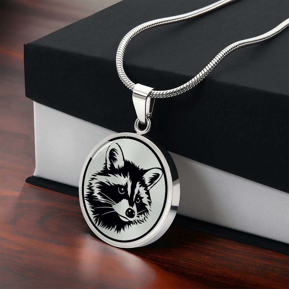 Raccoon necklace featuring a bold black-and-white raccoon face illustration with pointed ears and distinctive eye mask on a round silver-colored pendant with gift box