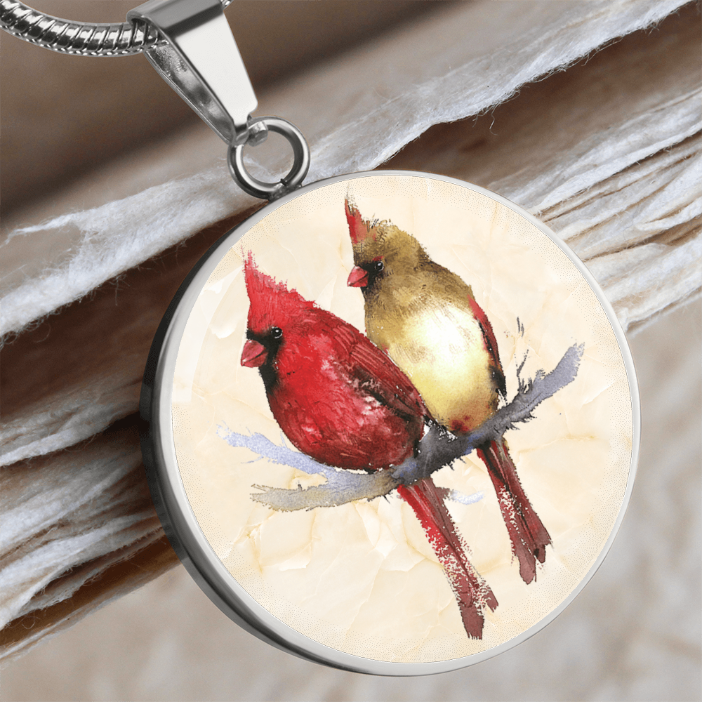 Northern Cardinal pair necklace showing a bright red male and golden-brown female cardinal perched together on a branch against a light watercolor background. mockup image with wooden background