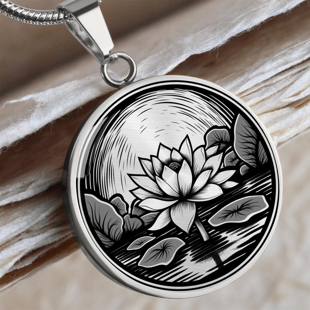 Silver finish lotus flower necklace featuring vintage linocut-style artwork of a blossom rising above a reflective pond.