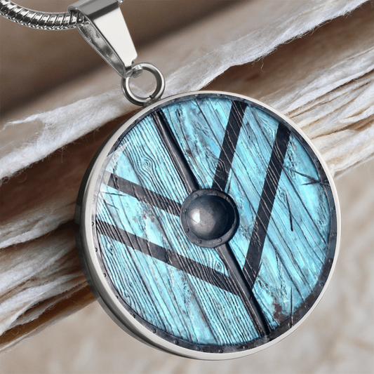 Viking shield necklace featuring a weathered turquoise-blue round shield with dark reinforcing bands and central metal boss on a circular pendant.