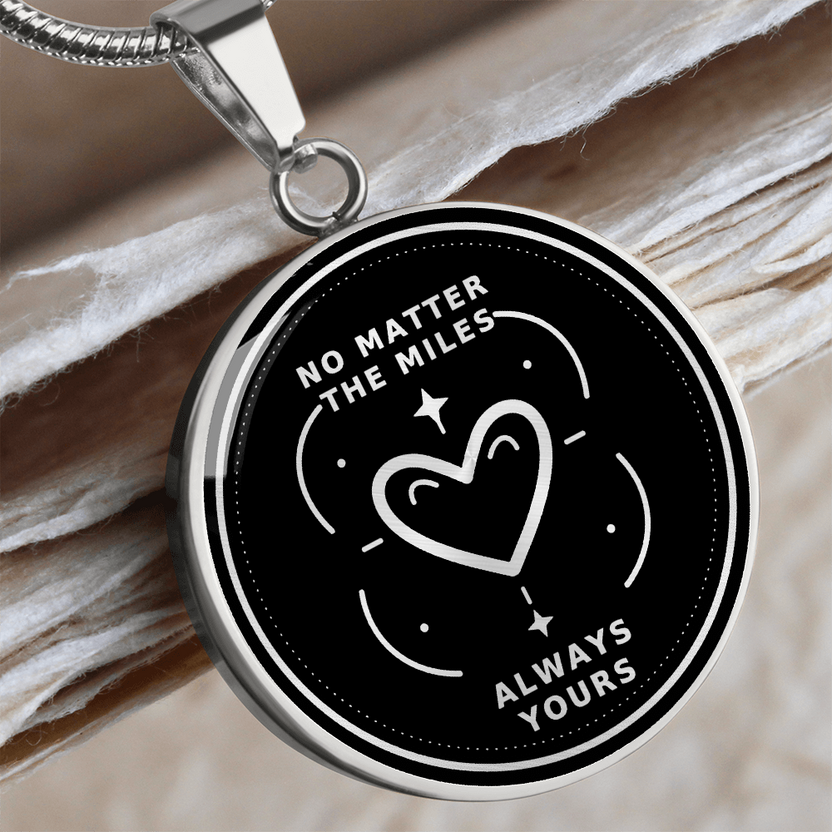 Silver No Matter the Miles necklace with white heart illustration and Always Yours lettering on a black circular pendant