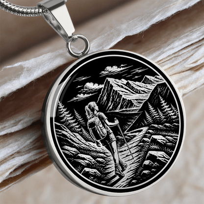 Woman hiking necklace featuring black-and-white linocut-style artwork of a female backpacker walking along a rocky mountain trail.
