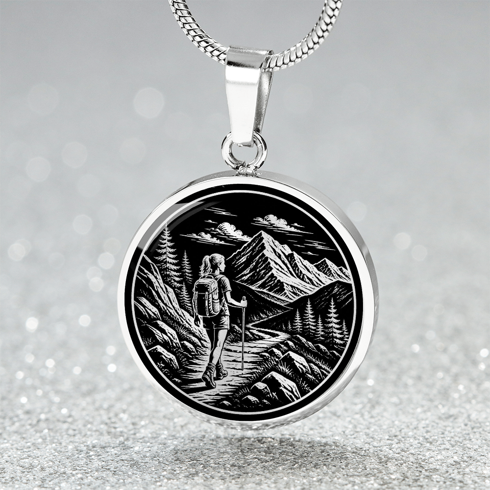 Woman hiking necklace featuring black-and-white linocut-style artwork of a female backpacker walking along a rocky mountain trail.