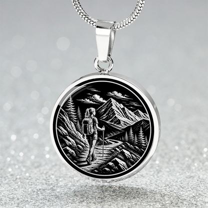 Woman hiking necklace featuring black-and-white linocut-style artwork of a female backpacker walking along a rocky mountain trail.