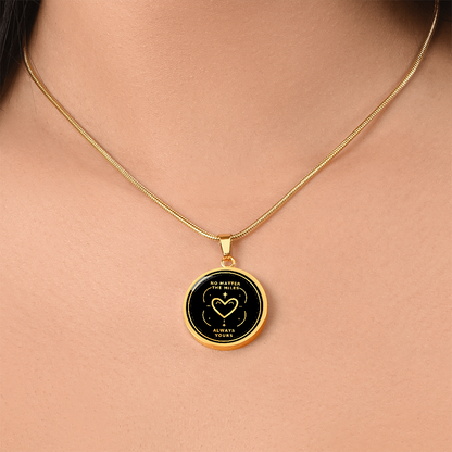 Gold finish No Matter the Miles necklace worn around the neck, featuring a circular black and gold Always Yours heart pendant.