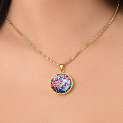 Woman wearinga gold Cherry blossom necklace featuring pink sakura flowers on dark branches against a turquoise-blue stained-glass-style circular pendant.