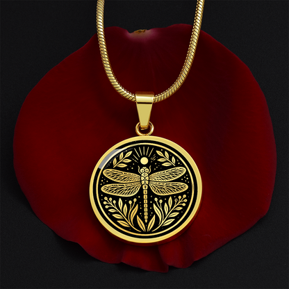 Dragonfly necklace with linocut-style artwork showing four patterned wings, botanical leaves and sun rays on a black circular pendant.