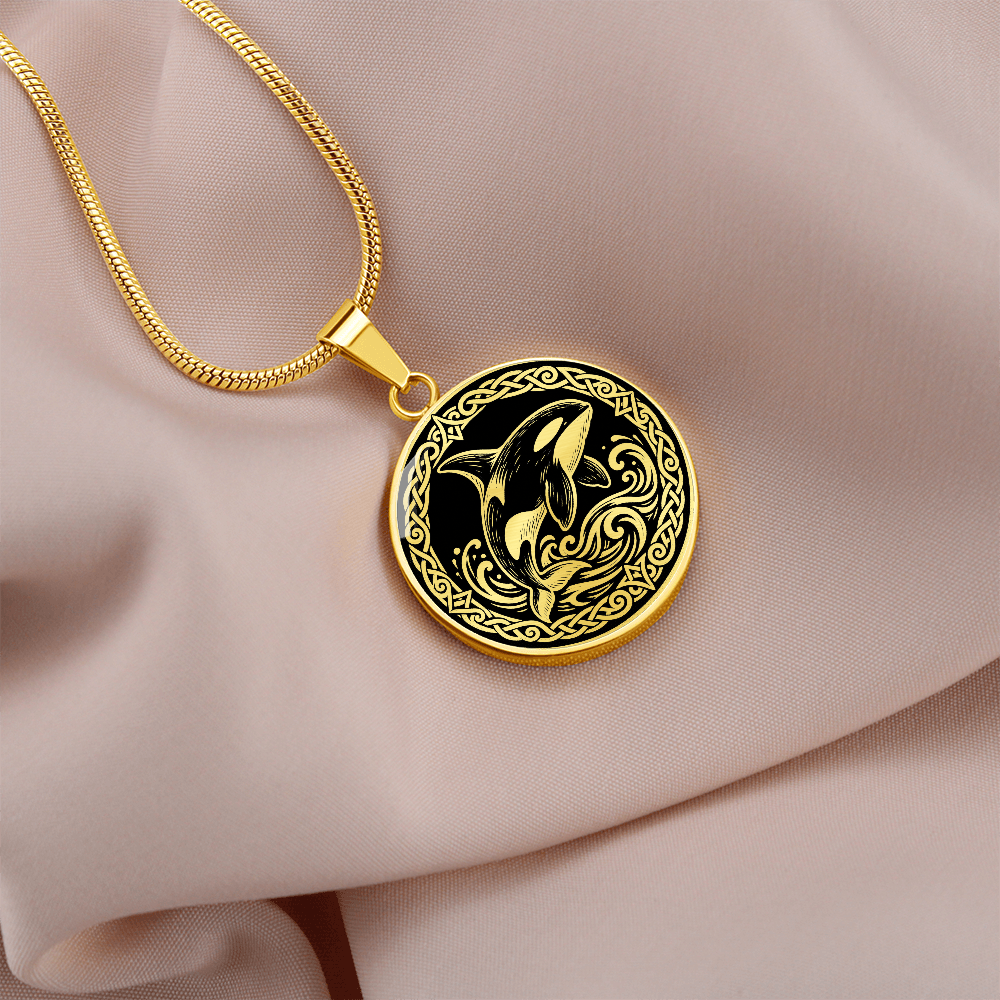 Gold orca whale necklace with decorative Viking-inspired border on pale fabric