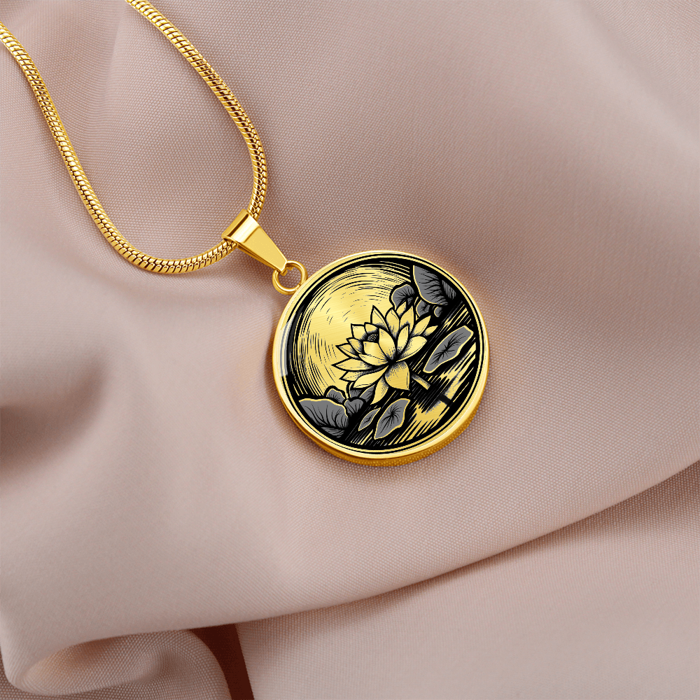Gold finish lotus flower necklace featuring vintage linocut-style artwork of a blossom rising above a reflective pond on a cream colored linen.