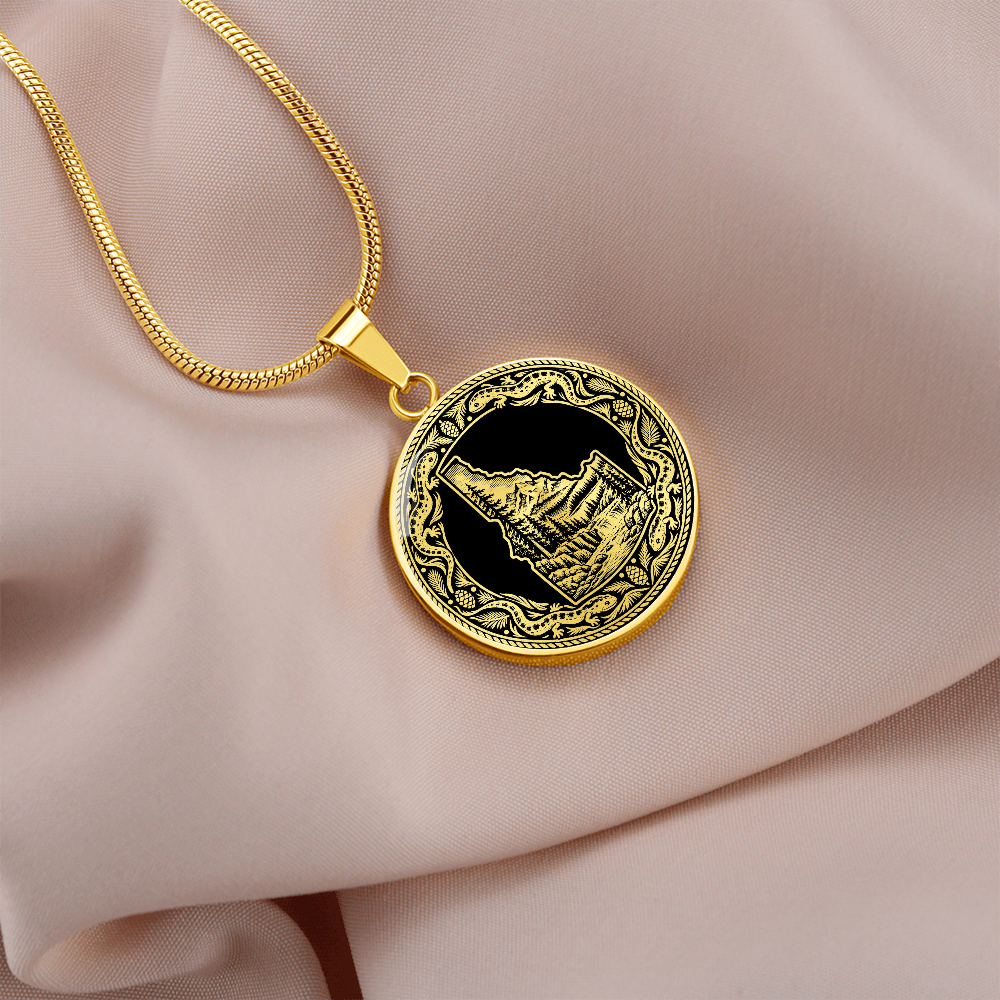 Gold finish Idaho state necklace featuring a black and white mountain wilderness illustration and decorative salamander-inspired frame