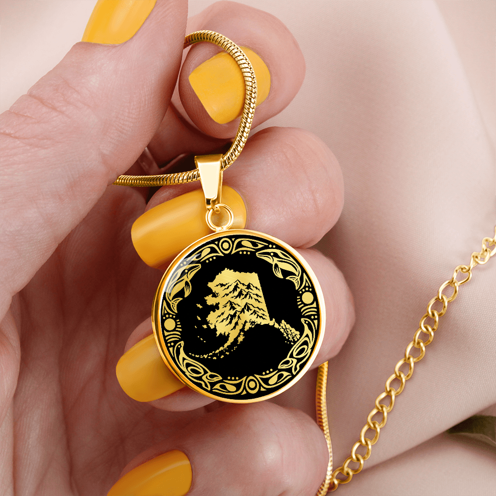 Gold finish Alaska mountain necklace with dramatic snowy peak illustration, black and gold linocut design and decorative border.