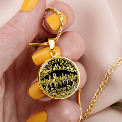 Gold finish San Diego skyline pendant with waterfront buildings, black and gold artwork and ornate city emblem border