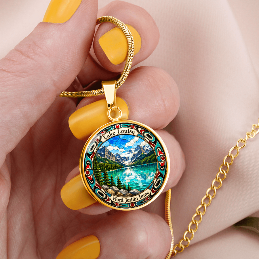 Gold finish Lake Louise pendant necklace held in a hand with bright turquoise mountain lake, snowy peaks, pine forest and stained-glass-style artwork