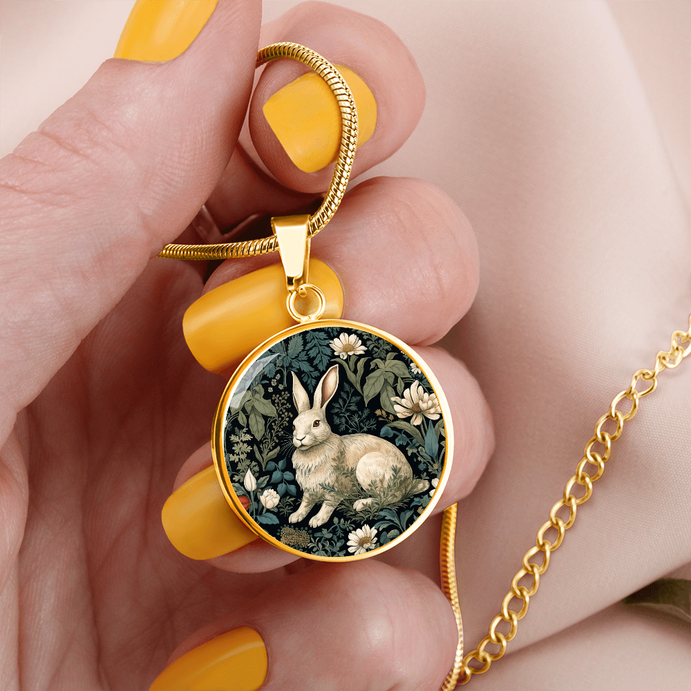 Woman holding a Botanical rabbit necklace featuring a cream-colored bunny surrounded by ivory daisies and sage-green foliage on a dark round pendant.