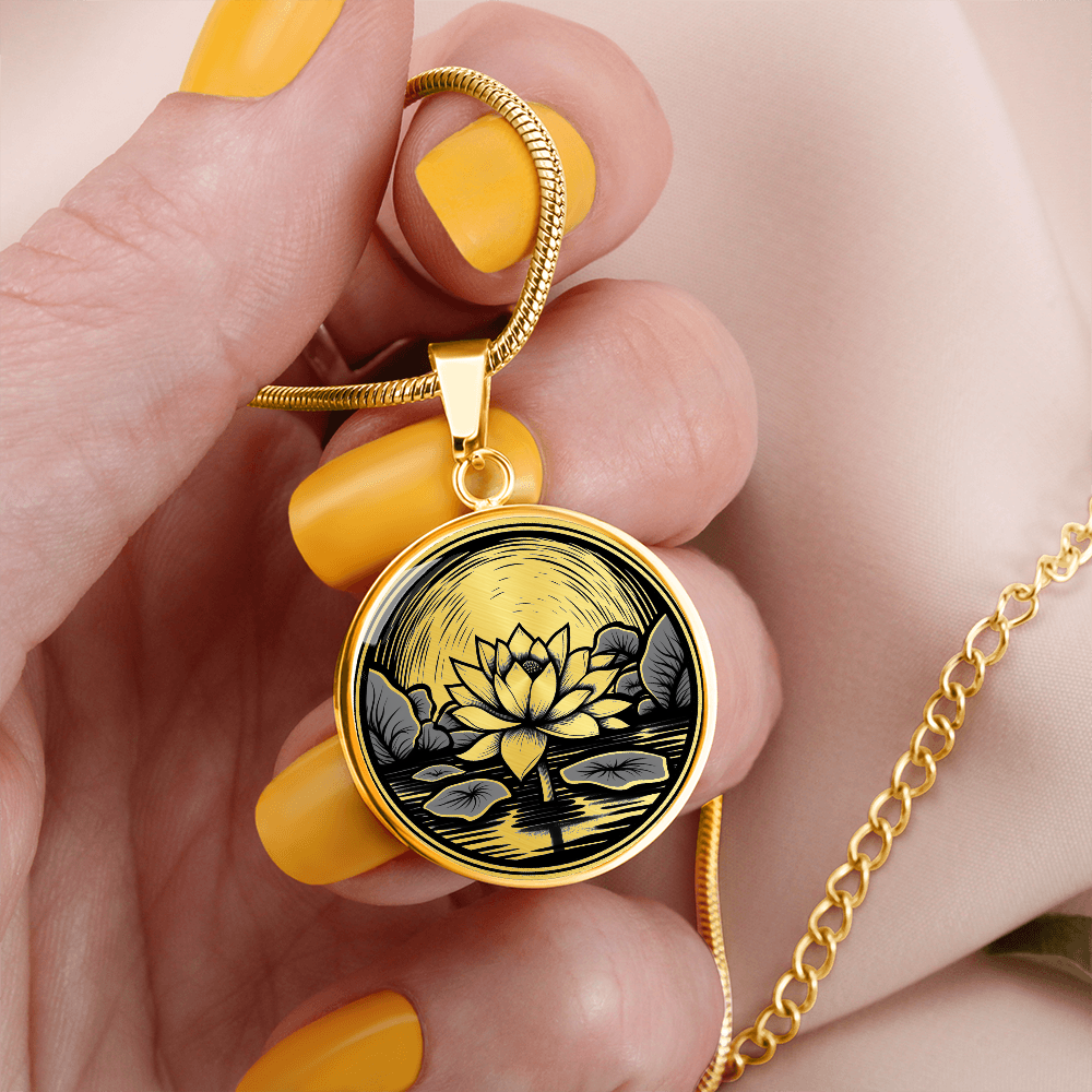Woman holding a Gold finish lotus flower necklace featuring vintage linocut-style artwork of a blossom rising above a reflective pond.