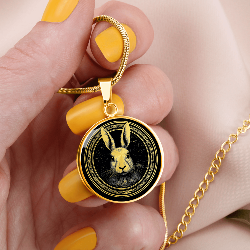 woman holding a gold William Morris-inspired rabbit necklace featuring a black-and-white rabbit portrait with long ears and ornate botanical border on a round pendant.