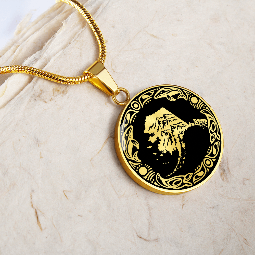 gold Alaska mountain pendant necklace featuring snowy peaks, black and white linocut artwork and an ornate circular border.